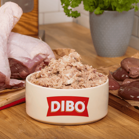 DIBO Finest raw food in a bowl on a wooden surface with raw meat and organs in the background.